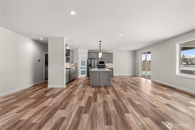 kitchen featuring pendant lighting, light countertops, gray cabinetry, open floor plan, and a kitchen island with sink