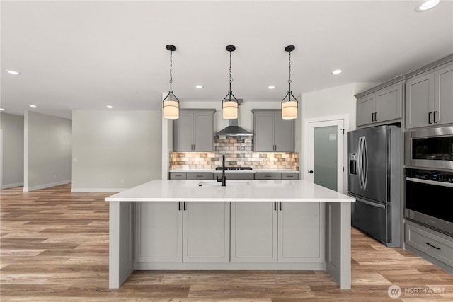 kitchen featuring stainless steel appliances, a center island with sink, gray cabinets, and light countertops