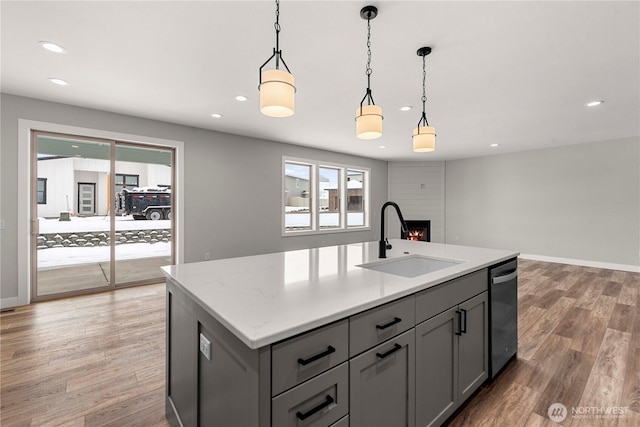 kitchen with a center island with sink, light stone countertops, gray cabinetry, pendant lighting, and a sink