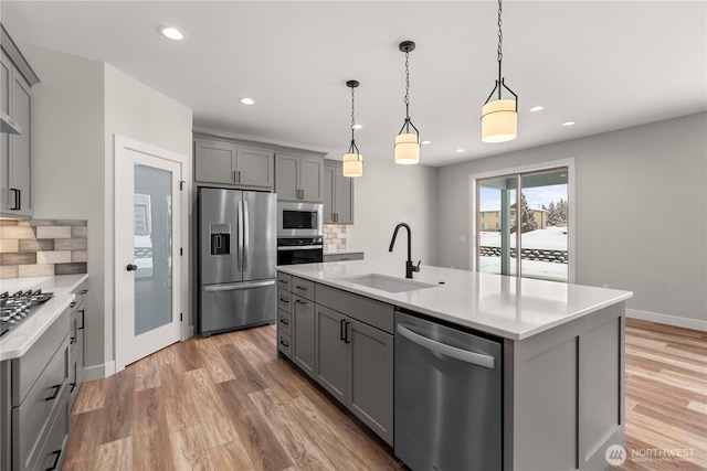 kitchen featuring stainless steel appliances, gray cabinets, light countertops, and a sink