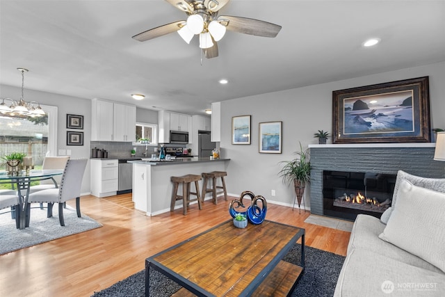 living room featuring light wood-type flooring, a fireplace with flush hearth, baseboards, and recessed lighting