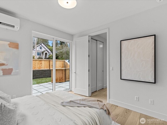 bedroom featuring access to exterior, an AC wall unit, light wood-style floors, and baseboards