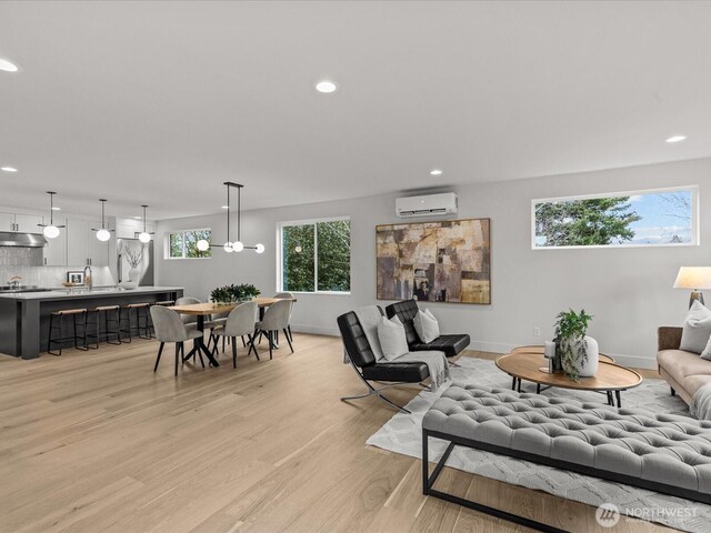 living room with a wall unit AC, light wood-style floors, baseboards, and recessed lighting