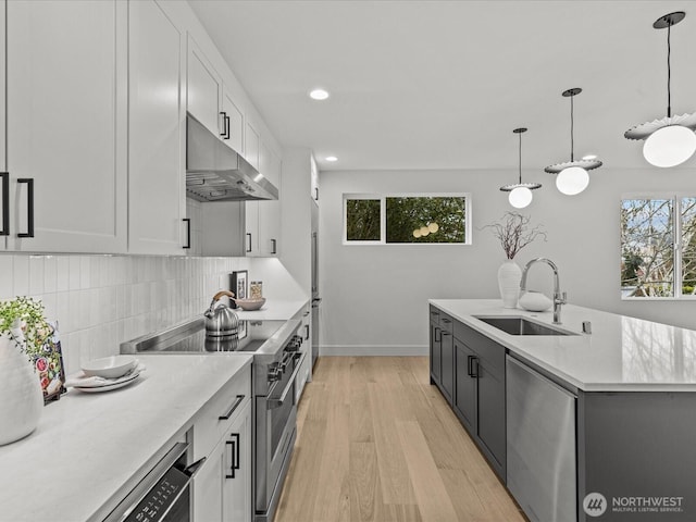 kitchen with under cabinet range hood, a sink, white cabinetry, appliances with stainless steel finishes, and pendant lighting