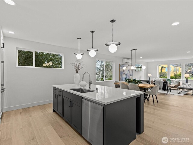 kitchen featuring a center island with sink, dishwasher, open floor plan, decorative light fixtures, and a sink