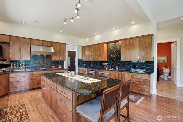 113 Northridge Dr, Ridgefield, WA 98642 - kitchen featuring light wood-style floors, stainless steel oven, a center island, a kitchen bar, and under cabinet range hood