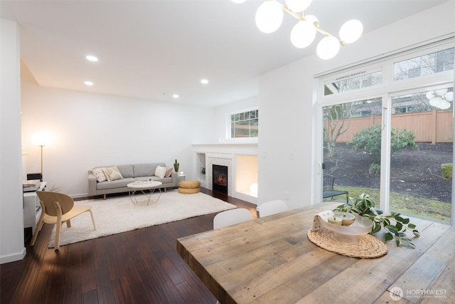 dining space with a chandelier, recessed lighting, dark wood-type flooring, baseboards, and a glass covered fireplace