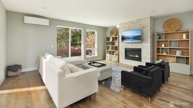 living room with a wall unit AC, a large fireplace, light wood-style flooring, and baseboards