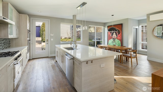 kitchen featuring glass insert cabinets, hanging light fixtures, a kitchen island with sink, light countertops, and a sink