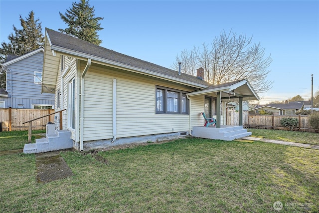 rear view of property featuring a lawn, a chimney, and fence