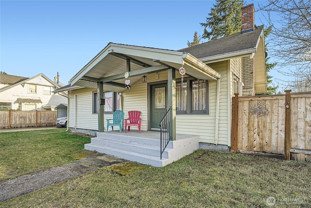 bungalow with a porch, a front yard, fence, and a chimney