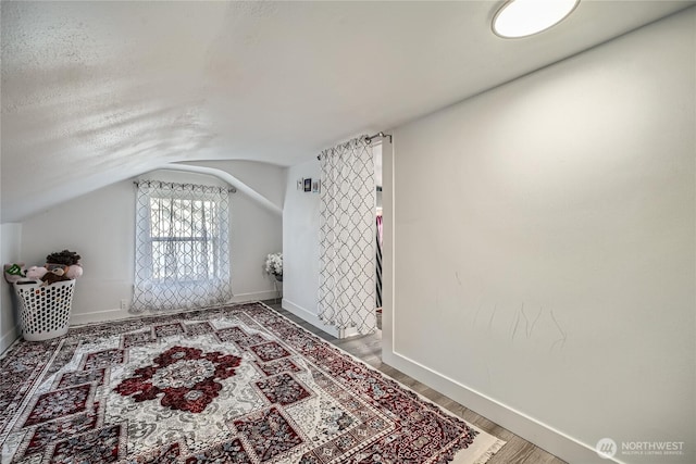 bonus room featuring lofted ceiling, a textured ceiling, baseboards, and wood finished floors