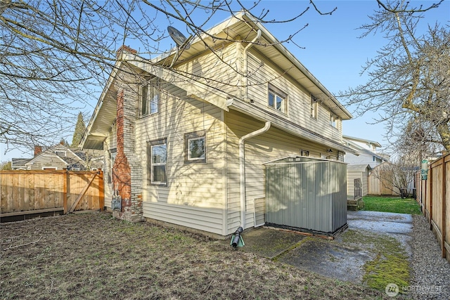 back of property with an outbuilding, a fenced backyard, a chimney, and a storage unit