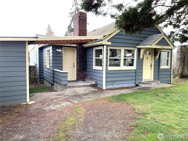 bungalow-style home with entry steps, a shingled roof, a chimney, and a front yard