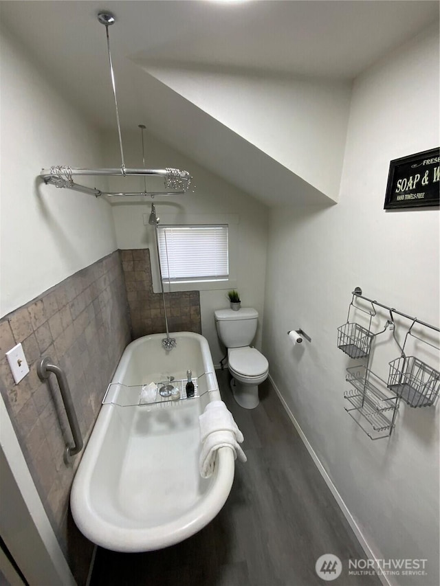 full bathroom featuring toilet, wood finished floors, baseboards, vaulted ceiling, and a soaking tub