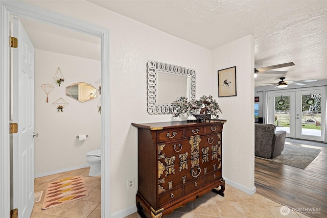 hall featuring light tile patterned flooring, baseboards, a textured ceiling, and french doors