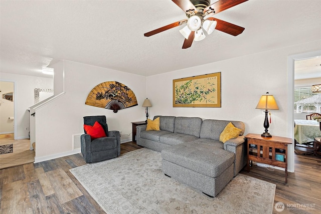 living room featuring ceiling fan, a textured ceiling, baseboards, and wood finished floors