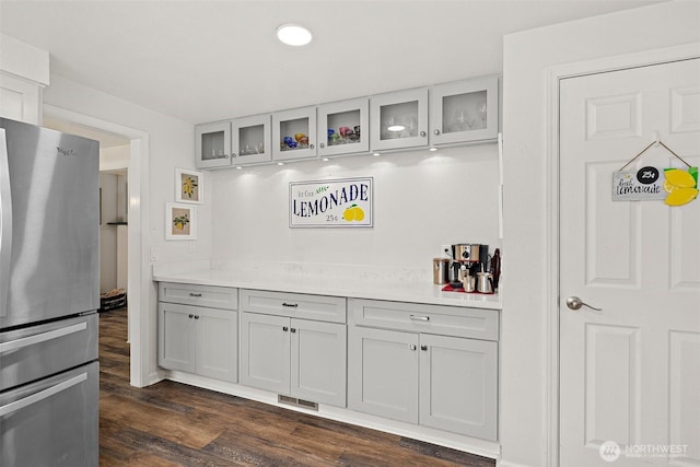 kitchen with dark wood-style floors, light countertops, visible vents, glass insert cabinets, and freestanding refrigerator