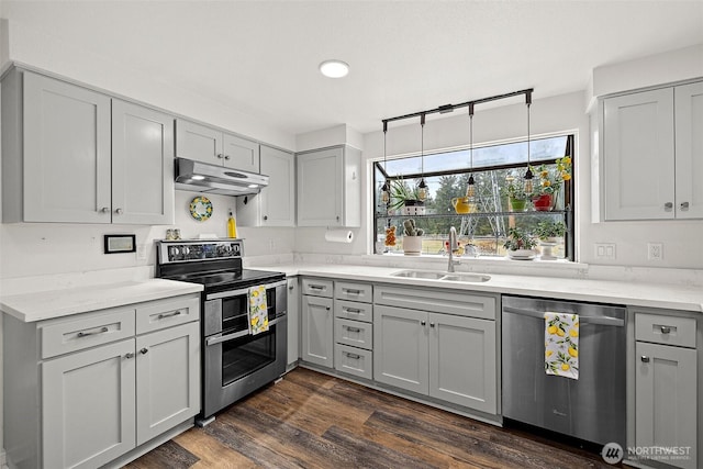 kitchen with dark wood-style floors, gray cabinets, stainless steel appliances, under cabinet range hood, and a sink