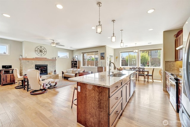 kitchen with an island with sink, light stone countertops, a stone fireplace, pendant lighting, and a sink