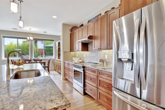 kitchen featuring light stone counters, under cabinet range hood, stainless steel appliances, a sink, and hanging light fixtures