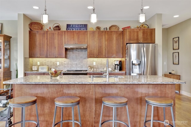 kitchen featuring appliances with stainless steel finishes, brown cabinetry, a sink, and a kitchen island with sink