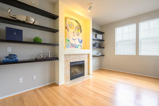 unfurnished living room with baseboards, a tile fireplace, light wood-style flooring, and built in features