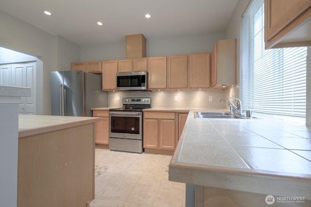 kitchen with tile countertops, a sink, stainless steel appliances, light brown cabinetry, and backsplash