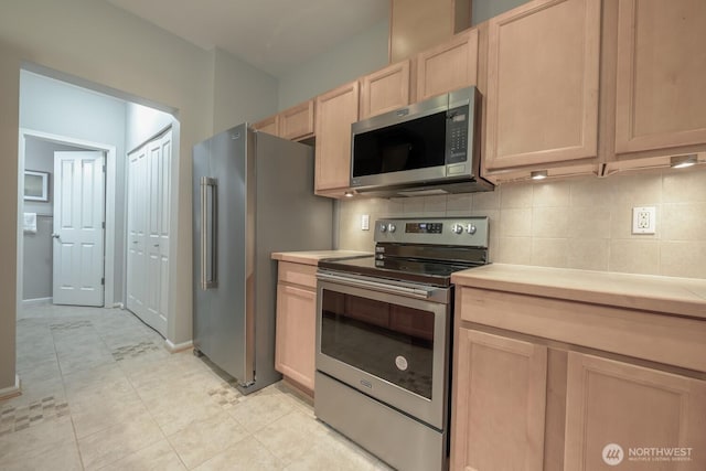 kitchen with light tile patterned floors, light countertops, appliances with stainless steel finishes, backsplash, and light brown cabinetry