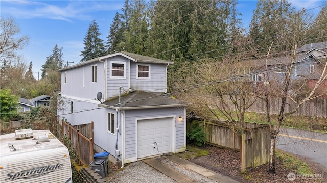 view of side of home featuring a garage, fence, and a shingled roof