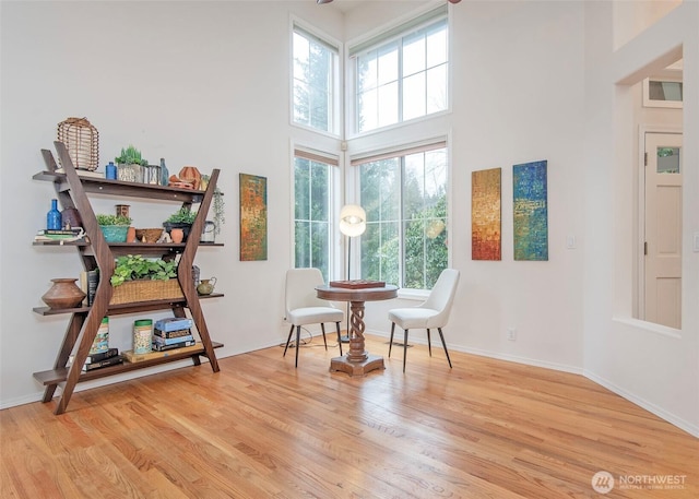 sitting room featuring light wood-type flooring, baseboards, and a high ceiling