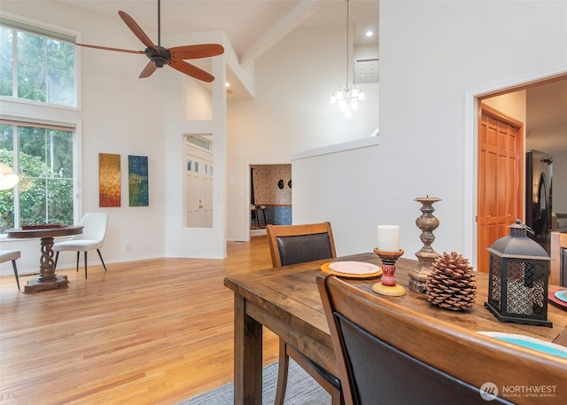 dining room featuring a towering ceiling, baseboards, wood finished floors, and ceiling fan with notable chandelier