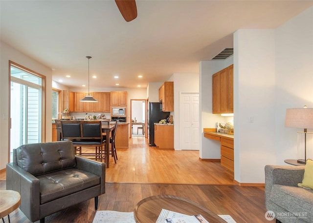 living room featuring light wood finished floors, recessed lighting, visible vents, built in study area, and baseboards