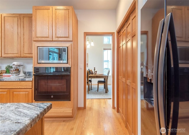 kitchen with black appliances, light stone counters, and light wood-style floors