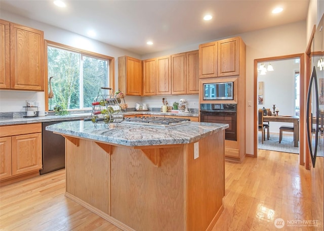 kitchen featuring light stone counters, a breakfast bar, stainless steel appliances, light wood-style floors, and a kitchen island