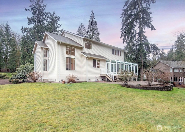 back of house at dusk featuring a sunroom, crawl space, and a lawn