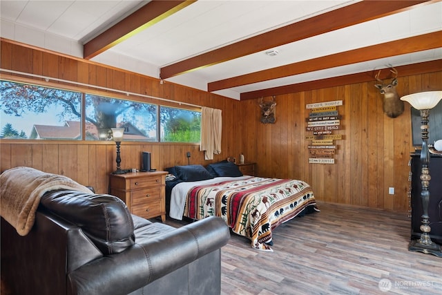 bedroom with wood walls, beam ceiling, and wood finished floors