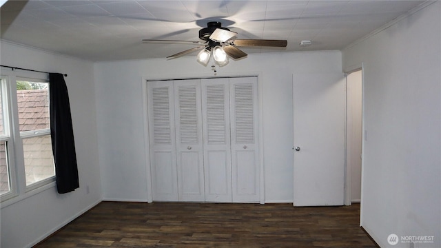 unfurnished bedroom featuring dark wood-type flooring, a closet, crown molding, and ceiling fan