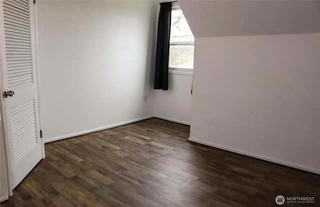 unfurnished bedroom featuring dark wood-type flooring, lofted ceiling, and baseboards