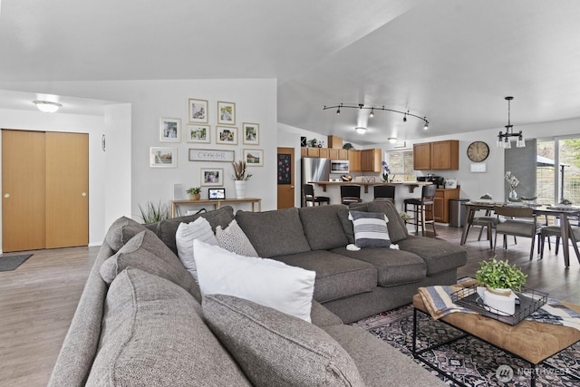 living room with a chandelier, lofted ceiling, track lighting, and light wood finished floors