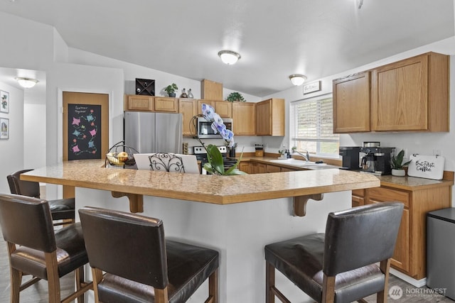 kitchen featuring lofted ceiling, appliances with stainless steel finishes, light countertops, a kitchen bar, and a sink