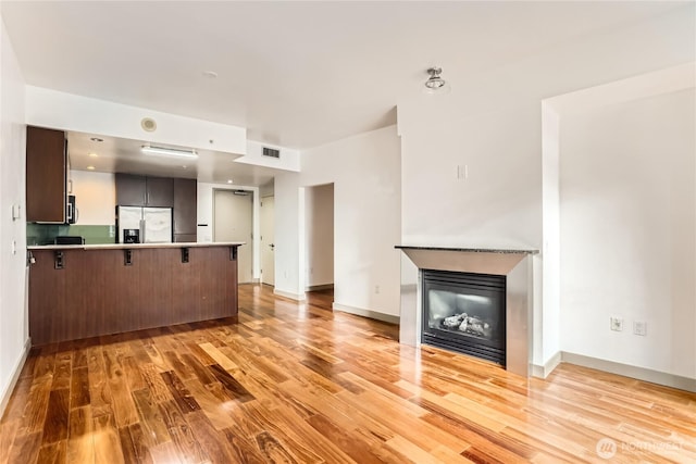 unfurnished living room with light wood finished floors, baseboards, visible vents, and a glass covered fireplace