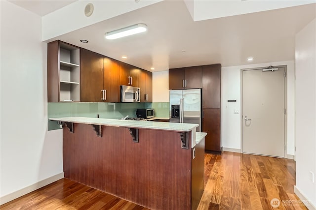 kitchen featuring a peninsula, a kitchen breakfast bar, light countertops, appliances with stainless steel finishes, and light wood-type flooring