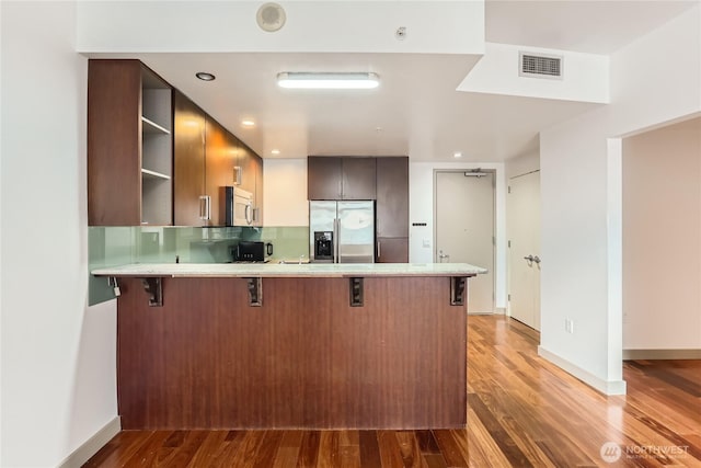 kitchen with a peninsula, a breakfast bar, light countertops, stainless steel fridge with ice dispenser, and modern cabinets