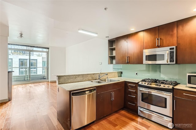 kitchen featuring a peninsula, a sink, appliances with stainless steel finishes, light wood-type flooring, and open shelves