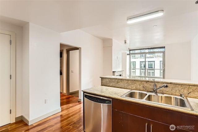 kitchen featuring wood finished floors, stainless steel dishwasher, a sink, light stone countertops, and baseboards