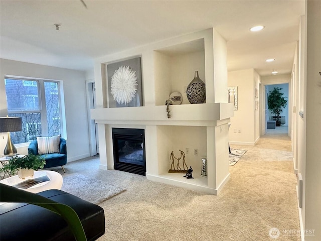 living area featuring recessed lighting, baseboards, a glass covered fireplace, and light colored carpet