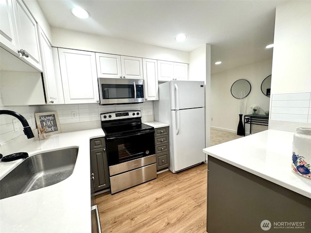 kitchen with tasteful backsplash, white cabinets, stainless steel appliances, light countertops, and a sink