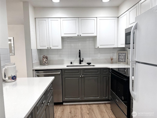 kitchen with light wood finished floors, light countertops, appliances with stainless steel finishes, white cabinetry, and a sink