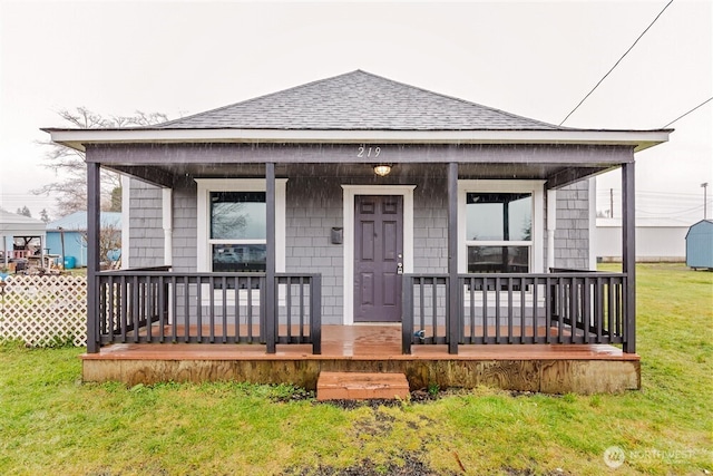 view of front facade featuring a shingled roof, a front lawn, and a porch